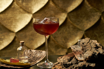 Fresh branded red alcoholic cocktail with a small bottle for alcohol and a red marmalade snack on a black stone bar counter.  Concept of alcoholic and non-alcoholic bar beverage.