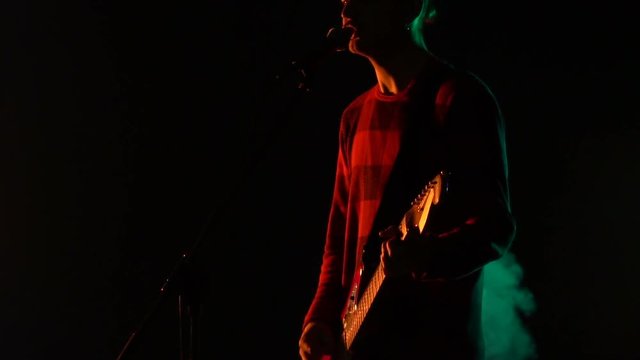 Hipster guy plays guitar and sings on stage in smoke. Slow motion. Music, Sound, Band, Concept.