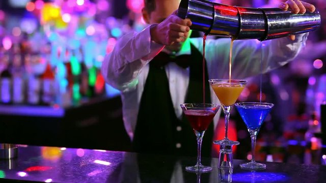 club: a bartender pours colorful cocktails 3 glasses at once.