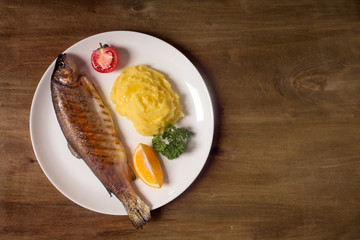 Grilled whole trout, potato, lemon and garlic, close up. Wooden background