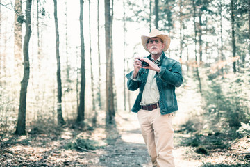 Photographer wearing straw hat and jeans jacket in sunny forest.