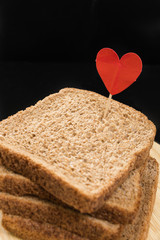 Whole grain sandwich bread slice with heart pin, with dark background.