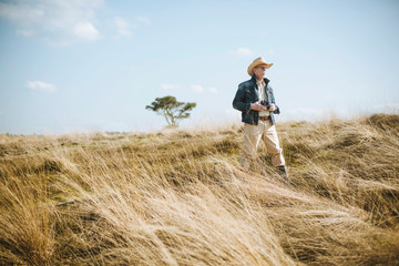 Naklejka na ściany i meble Man with hat and camera in field on safari.