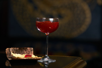 Fresh branded red alcoholic cocktail with a small bottle for alcohol and a red marmalade snack on a black stone bar counter.  Concept of alcoholic and non-alcoholic bar beverage.
