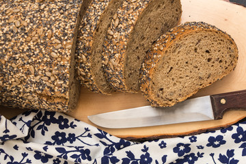 Whole wheat sliced bread closeup , on wooden surface with floral kitchen towel and knife