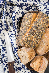 Whole wheat sandwich buns, on wooden dish with floral kitchen towel and knife.