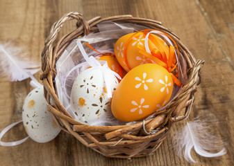 Easter eggs decorated in a basket with feathers on wooden background