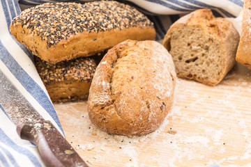 Whole wheat bread buns and slices, on wooden surface with flour.