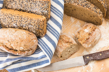 Whole wheat bread buns and slices, on wooden surface with flour.