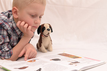 A five-year-old boy is reading a book on the bed.
