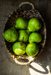 Ripe green organic pears in vintage wicker basket on weathered wood kitchen table, sunlight flecks