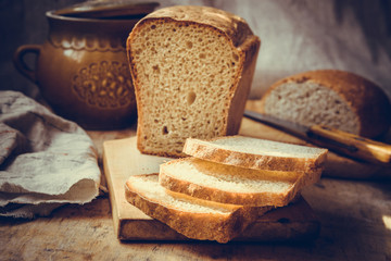 Sourdough bread loaf, sliced on old wood cutting board, vintage crockery, linen towel, authentic rural style, still life