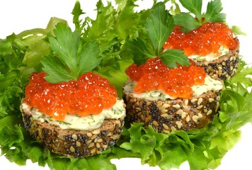 Sandwiches with red caviar, made from black baguette sprinkled with grains of cereals and poppy, lie on green leaves of salad