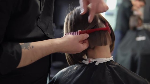 Closeup view of a barber cutting hair of young woman in professional hair salon. Beauty and haircare concept. Shot in 4k