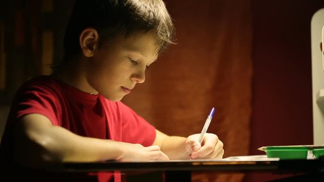 The boy at the desk writes in a notebook