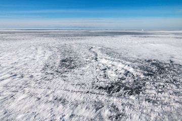 Frosen sea under ice and snow shaped by wind against blue sky.