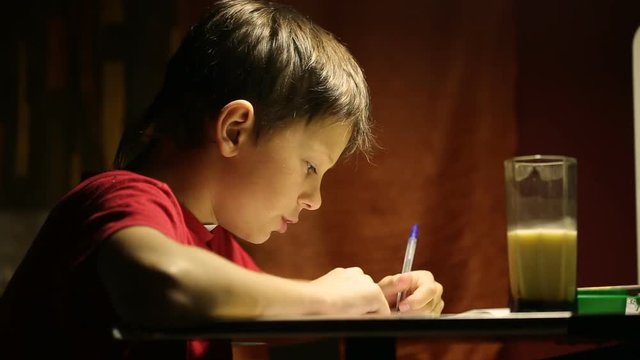 The boy at the desk writes in a notebook