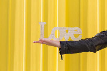 young woman arm holding  LOVE Word over yellow background. Casual clothing