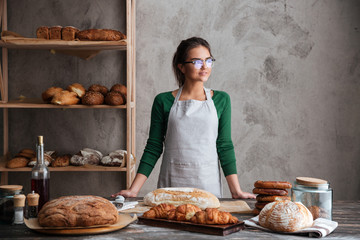 Amazing young lady baker standing at bakery near bread - obrazy, fototapety, plakaty