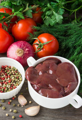 Raw chicken liver with tomatoes and herbs on a wooden table.