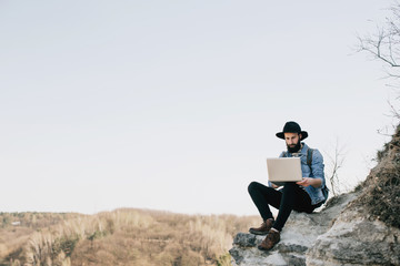 handsome bearded man freelancer working on a laptop outdoors in mountains. Freelance concept