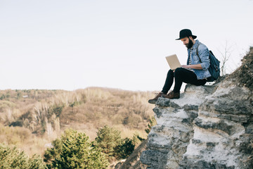 handsome bearded man freelancer working on a laptop outdoors in mountains. Freelance concept - obrazy, fototapety, plakaty