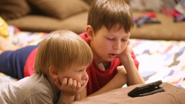 Children in pajamas watch cartoons on the phone