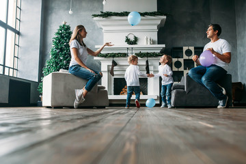 Father and mother siting on sofa playing air balloons with two little sons