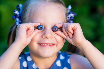 Smiling girl showing blueberries in front of her face - covering her eyes with blueberries