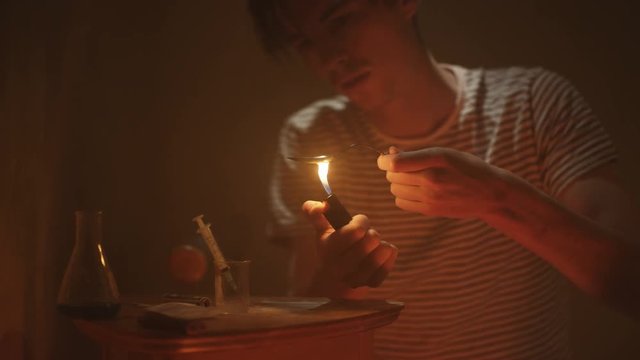  Drug addict in gloomy apartment preparing & injecting heroin into arm