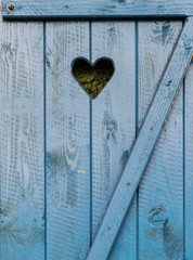 Heart shaped hole carved into vintage blue wooden window shutter 