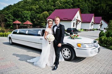 Stylish wedding couple against wedding limousine.