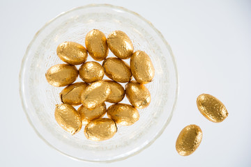 High angle view of a variety of golden wrapped  Easter chocolate eggs on a plate and white background