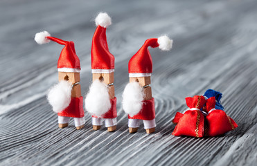 Fototapeta premium Xmas greeting card with group funny toy clothespin Santa, red gift bags on beautiful wooden background. christmas poster creative design. Macro view shallow depth field.
