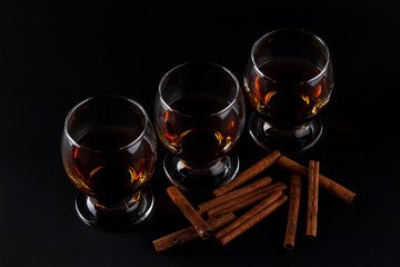 Glasses of cognac and cinnamon sticks on a black background