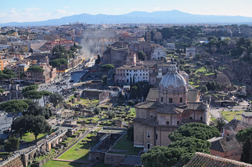 Fototapeta premium View to rooftops of Rome skyline from the Monument of Vittorio Emanuele II at Piazza Venezia. Rome Forum with ruins of historical buildings. Colosseum in the background. Winter morning view