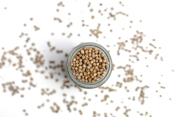 Organic Dried coriander seeds (Coriandrum sativum) in a glass jar, selective focus, on white background
