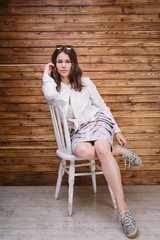 a young girl with long hair, white clothing, on a chair and wooden background