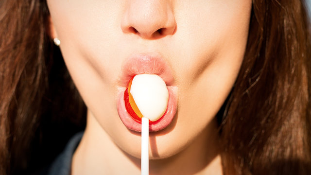 Close-up of a girl sucking a candy on a chupa chups sticking a candy with her lips