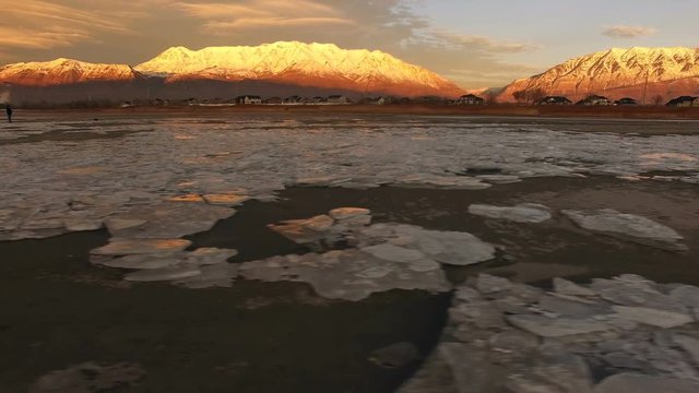 Panning view of ice chunks on shore of lake reflecting snow capped mountain