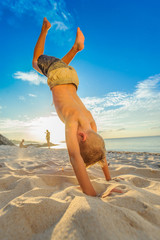 Handsome eight years boy on beach performs acrobatic sketches and plays with a stream of sand