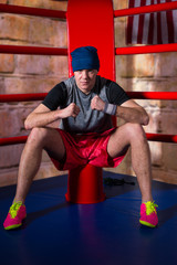Fototapeta premium Athletic young male boxer sitting near red corner of a regular boxing ring
