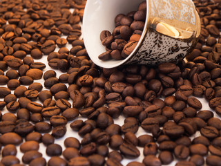 Scattered coffee beans with inverted oriental cup over white background