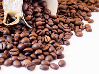 Scattered coffee beans with inverted oriental cup over white background