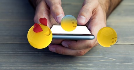 Hands holding mobile phone with various emojis 