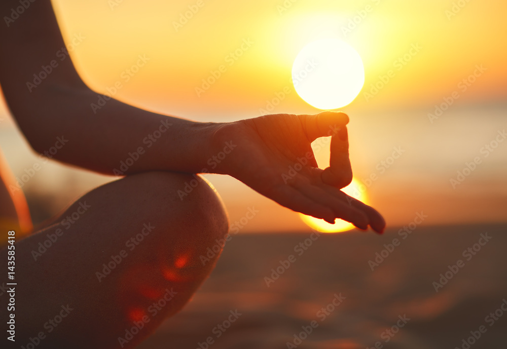 Wall mural hands of woman meditating in yoga pose at sunset on beach