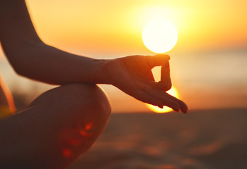 hands of woman meditating in yoga pose at sunset on beach