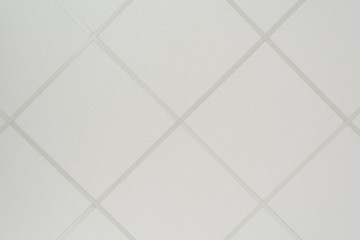 The texture of a false ceiling consisting of square plates and a directing profile of the diagonal arrangement, an abstract white background