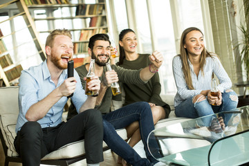 Group of young friends looking at the TV, drinking cider and having fun  in the room