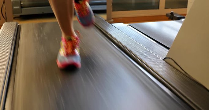 Woman feet in colorful shoes running on treadmill machine in gym. Fitness center training. Aerial and side view. Healthy lifestyle concept. 4K close up.